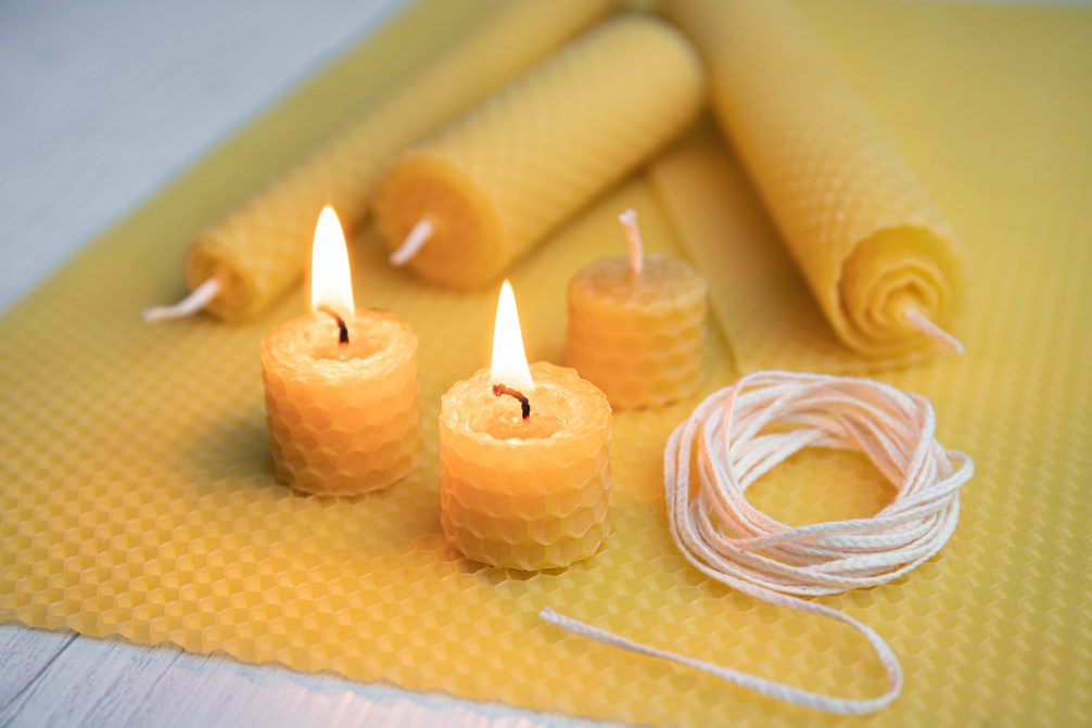 Natural rolled beeswax candles from pressed beeswax honeycomb sheet at home indoors. Hobby concept. Two candles lit and burning.
